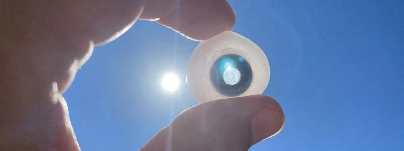 Primer plano de una persona sosteniendo un ojo artificial translúcido con el iris azul hacia un cielo despejado. La luz del sol se filtra a través de la prótesis ocular, destacando los detalles de su diseño y simetría en un contexto de salud visual y superación.