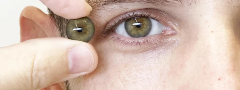Una mano sostiene una cascarilla ocular junto al ojo sano de una persona para comparar el color pardo del iris y el acabado realista